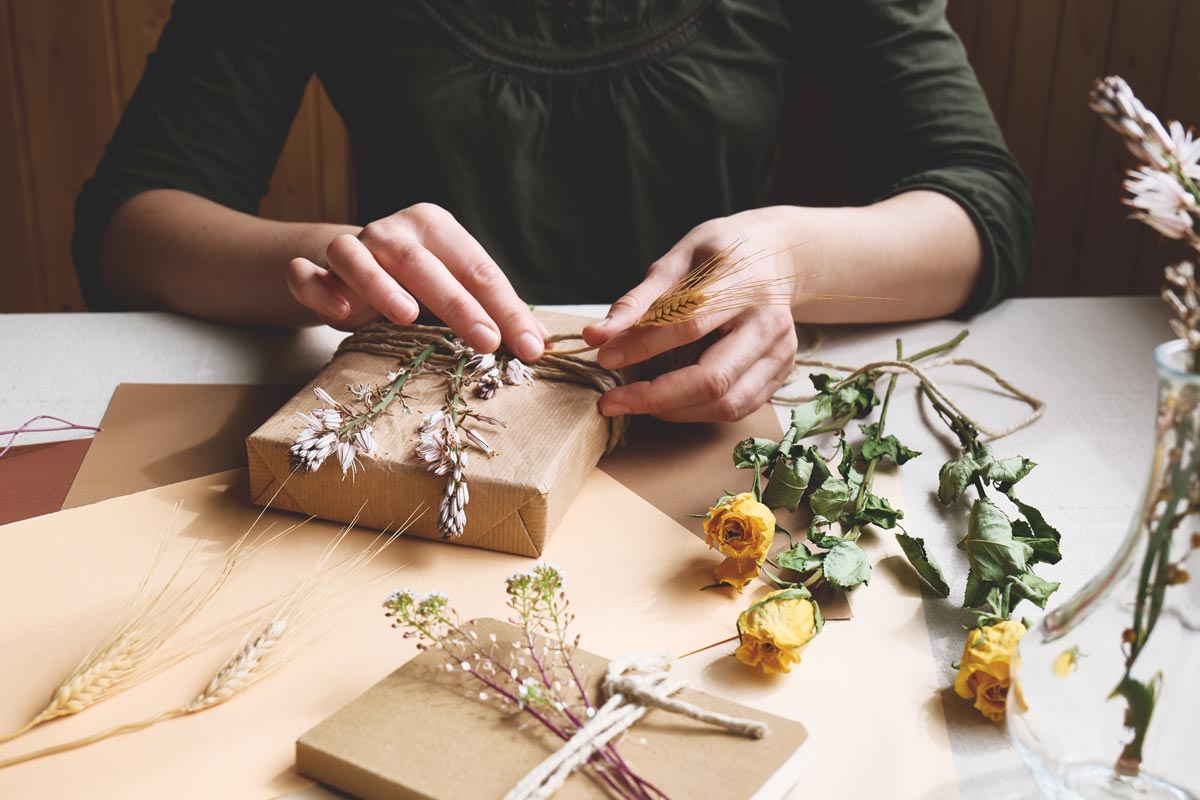 woman's hands tying dried flowers onto a brown paper wrapped gift
